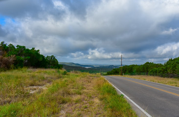 Fototapeta na wymiar Open Road in the hill country underneath clouds and open sky.