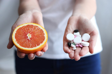 Female hands with citrus and different pills on a light background. Choose between the traditional...