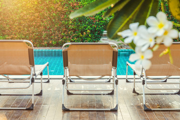 Rear view of sun loungers on decks at the side of swimming pool. For relaxation and recreation in hotel resort.