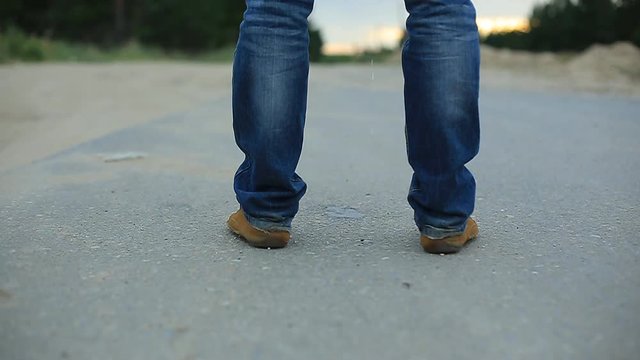 a man pees on the asphalt country highway. male legs in jeans and brown shoes.