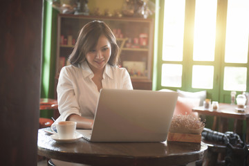 Asian girl wearing a white shirt playing a tablet in a cafe in the morning