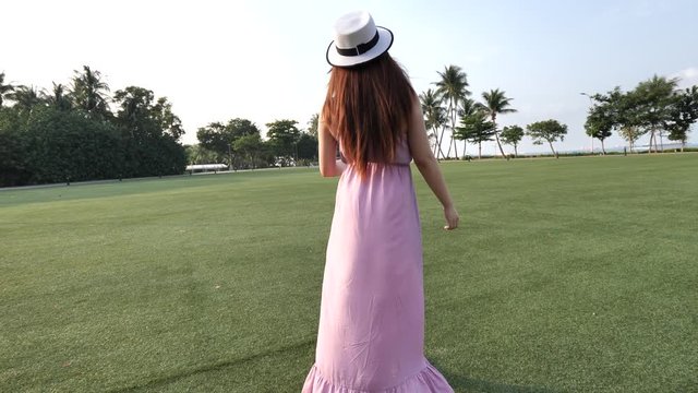 Asian chinese woman with hat walking across green lawn