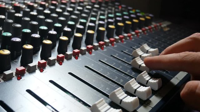 Man control fade sliders on audio mixer console desk in music studio indoors