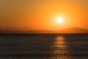 Sunrise over the sea and mountains on the horizon.