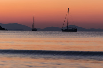 Two single yachts at sea during sunrise in the early morning.