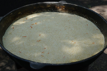 Cooking of pilaf in a large outdoor cauldron in a summer park