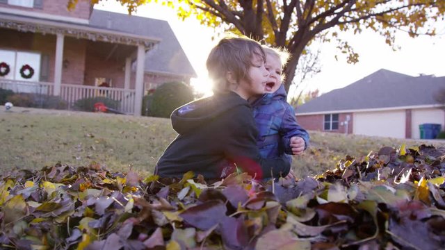 5 year old boy comforts grumpy toddler, who pushes him away with lens flare