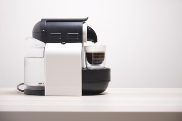 Coffee espresso capsule machine maker and glass against plain neutral background