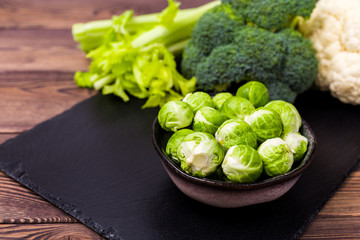 Close up of assorted healthy fresh vegetables on a black slate on a wooden table: cabbage, broccoli, cauliflower and Brussels sprouts and celery.