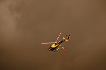 Elicottero giallo di soccorso alpino vola attraverso una nube di fumo di colore seppia