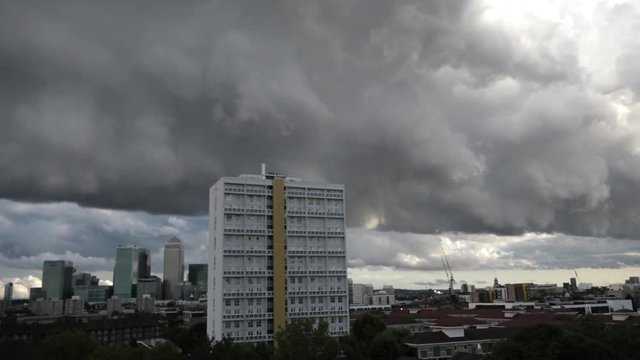 UK August 2018 - time lapse of a dark and menacing storm cloud rolling over a white tower block and London Canary Wharf financial district in the background.