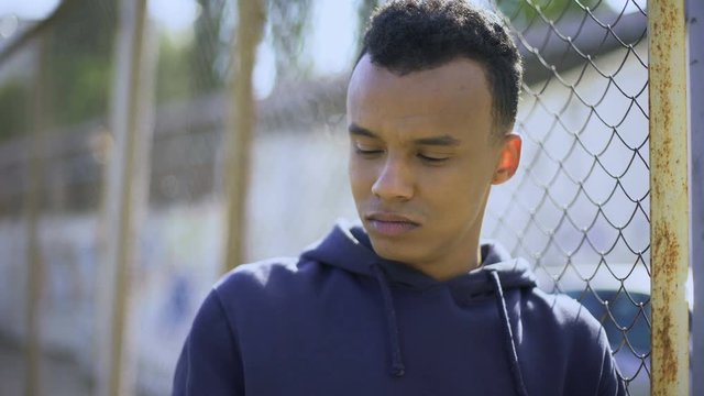 Afro-american boy leaning on fence, young refugee from dysfunctional family