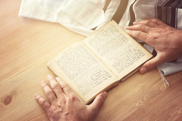 Fototapeta na wymiar Jewish man hands holding a Prayer book, praying, next to tallit. Jewish traditional symbols. Rosh hashanah (jewish New Year holiday), Shabbat and Yom kippur concept.