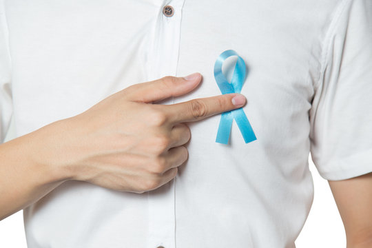 Men's healthcare concept - close up of male hand pointing to light blue ribbon for prostate cancer at left chest isolated on white background.
