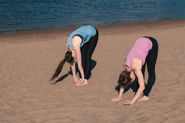 Two woman doing yoga on the beach by the river in the city. Beautiful view.