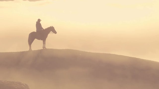 Horseman standing at fog covered mountain cliff waiting for tourist at sunrise, timelapse clip, Bromo