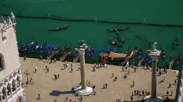 Columns of Saint Mark - Column of Lion and Saint Theodore of Venice, people walking between the columns near traditional venetian boats called gondolas.