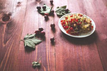 Berries of a currant, gooseberries on a saucer, leaves, on a natural wooden background