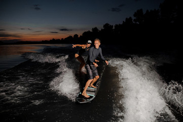 Couple of wakesurfers riding down the blue river at the evening