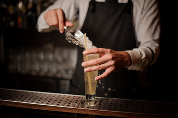 Barman adding ice into a glass with sour summer cocktail