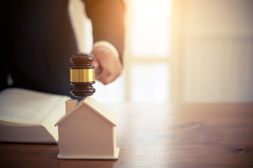 Hand with judge gavel and house model judge mediating in a property dispute in court or auctioneer...