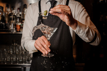 Barman holding a splashing fresh and strong summer martini cocktail with olive