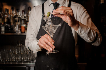 Barman holding a fresh and strong summer martini cocktail with olive