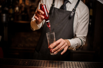 Barman adding red berry syrup into a cocktail glass