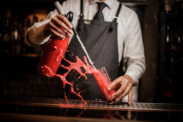 Barman pouring alcoholic sparkling water into a sweet red berry summer cocktail and splashing around