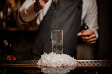 Barman adding some drops of brown bitter into a cocktail glass