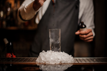 Bartender adding some drops of brown bitter into a cocktail glass