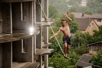 Active fearless man walking on a slackline and raising hands up