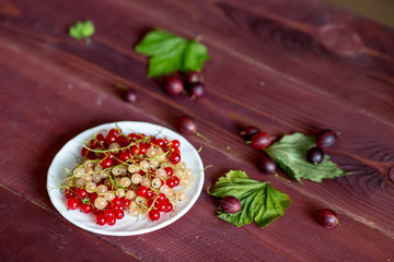 Berries of a currant, gooseberries on a saucer, leaves, on a natural wooden background