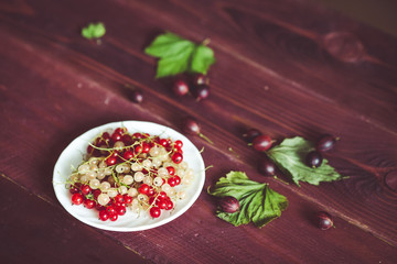 Berries of a currant, gooseberries on a saucer, leaves, on a natural wooden background