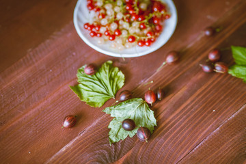 Berries of a currant, gooseberries on a saucer, leaves, on a natural wooden background