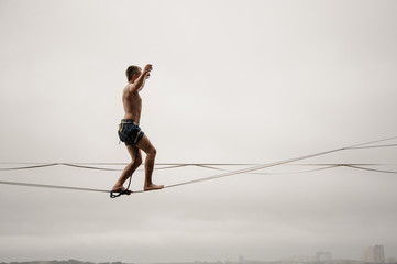 Brave man walking on a slackline against the grey sky