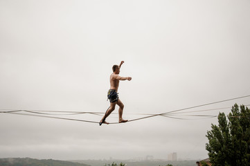 Strong and brave man walking on a slackline against the grey sky