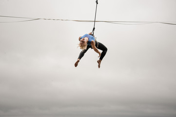Fearless blonde woman balancing on a slackline against the grey sky