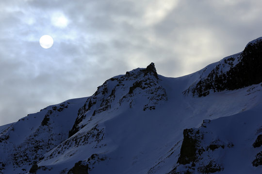 Round Sun in Cloudy Sky, over a Snowy Ridge. Svalbard, Norway
