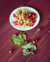 Berries of a currant, gooseberries on a saucer, leaves, on a natural wooden background