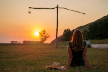 Young woman sitting in a field close to an old well at sunset