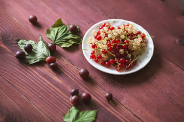 Berries of a currant, gooseberries on a saucer, leaves, on a natural wooden background