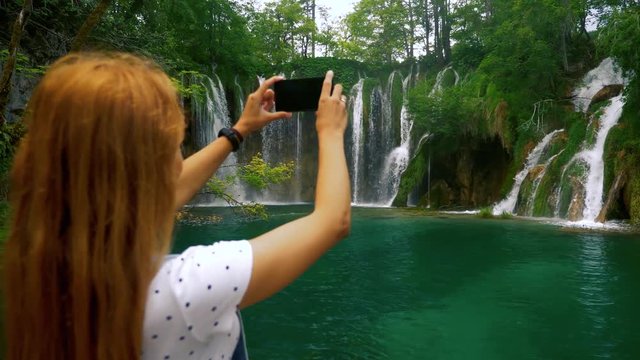 Tourist woman taking travel photos of a beautiful waterfall.