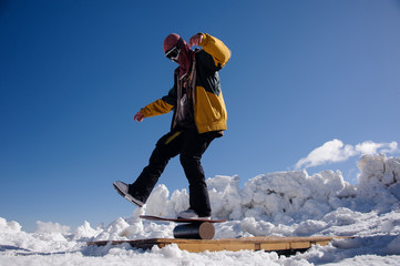 man in ski equipment and safety glasses balances on a snowboard