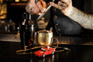 Fototapeta na wymiar Barman hands with tattoo and rings rubbing nutmeg on grater into copper mug