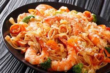 Pasta fettuccine with squid, tiger shrimps, vegetables, parmesan cheese and tomato sauce close-up on a plate. Horizontal