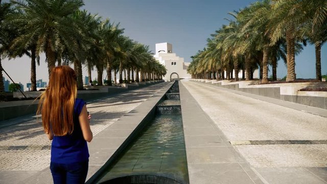 Tourist woman taking photos to palm trees and big building in middle east.