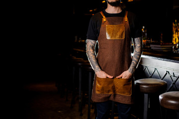 Bartender with tattoo dressed in brown apron