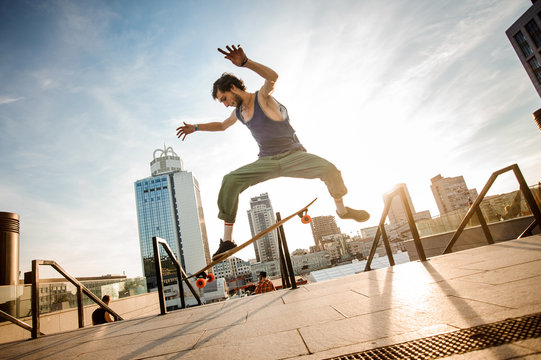 Active young man jumping on skateboard against the city buildings and sky