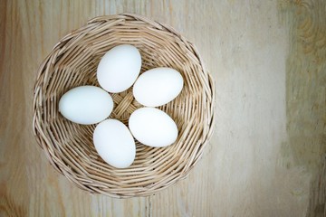 5 eggs in rattan basket on wooden background, lighten center